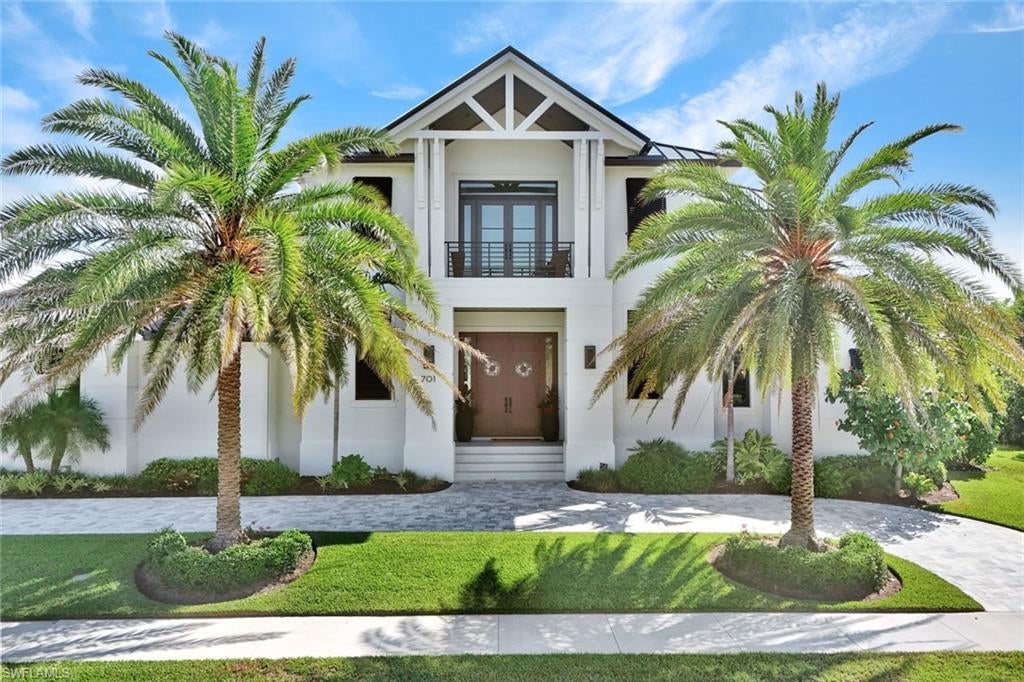 Sitting on a quiet corner within the Marco Beach enclave with direct frontage on a navigable waterway, this newer construction built by award winning R.K. Reiman Construction defines how an island residence should be lived in. Framed by royal palms, the gabled front elevation gives way to an interior defined by linear coffered ceilings that draw the eye toward the water through a wall of pocketing sliders, with wide-plank luxury vinyl flooring carried throughout. Considered the heart of the home, the kitchen is anchored by a double-waterfall edged island that
could seat plenty along its working edge, with induction cooking, custom cabinetry, Sub Zero, Wolf, and Miele appliances, and a hidden pantry that absorbs the demands of entertaining without compromising the main living area. A wet bar with glass shelving and an undermount Subzero wine cooler supports the adjacent dining area. The expansive sliding glass doors give way to a covered lanai with tongue-and-groove ceiling
that seamlessly extends the great room into a year-round living space, and is complete with a fully equipped outdoor kitchen, automatic hurricane shutters, and roll down screens. Beyond, a heated pool, spa, and sun shelf rest on a deck framed by mature landscaping, and fire pit area. Tucked away for the utmost privacy, the ground-level primary suite places the daylight, pool, and dock within a single sequence of doors, and features dual dressing rooms, as well as a bath hosting an expansive walk-through shower and dual vanities. Additional quarters on the
ground level include an en-suite guest room with lanai access and additional room currently used as a study. Upstairs, the home opens into a second living space that could be utilized as a media room, recreation room, or fitness studio, with a covered balcony commanding water views. Completing the second level, two guest suites are configured as full en-suites, each with their own view orientation and walk-in closets. The property also features a Control4 whole-home music and lighting system. The property's deeded dock includes a boat lift, water, and electricity, with deep water access and immediate proximity to the open Gulf. Located near shopping, dining, and entertainment, including Veterans' Park, the property offers the rare convergence of tranquility and accessibility.