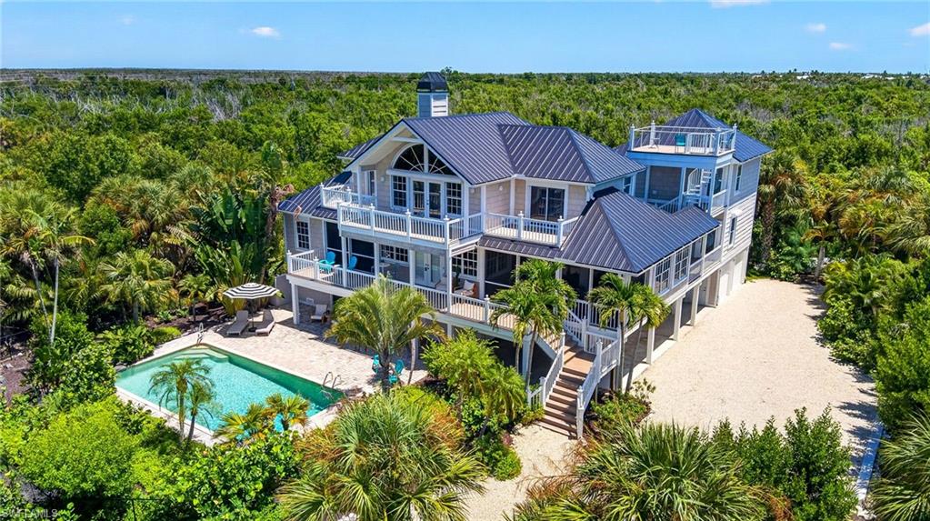 On 1.134 acres in Gulf Ridge on Sanibel Island, this property combines generous indoor and outdoor living with multiple deeded beach accesses, including a golf cart-accessible beach path. A new four-seat E-Z-GO golf cart is included with the sale, providing an easy connection between the residence and the Gulf. A notable feature is the attached guesthouse, an uncommon offering on Sanibel Island. Designed with two separate studio apartments, each with its entrance and studio kitchen, the guesthouse provides additional space for visiting guests or live-in caretakers. The studios also offer flexibility to be reimagined for uses such as a private office. A breezeway connects the guesthouse with the main residence and rooftop sundeck, creating separation while maintaining a cohesive connection between the spaces. Two additional garage bays are incorporated into the guesthouse. The main residence offers three bedrooms, two full baths and one half bath, including two primary suites, one on each level. Each suite opens to a private deck and includes a walk-in closet designed by California Closets. The upper-level primary suite features vaulted ceilings accented with tongue-and-groove wood planks. Solid plank pine floors stained in a pecan finish add natural character throughout the interiors. In the kitchen, natural wood cabinetry is paired with quartz countertops and stainless steel KitchenAid appliances, including a six-burner gas range. A gas fireplace wrapped in decorative quartz slab creates an architectural focal point in the living area. Outdoor living extends across composite decks to a pool with waterfall and two outdoor showers. Above, the spacious rooftop sundeck offers Gulf views and ample room for a furnished outdoor living area. Along the property's edge, a retaining wall directs rainwater toward designated retention areas to support overall drainage. The main residence provides a two-car garage, golf cart garage and covered carport. Following Hurricane Ian, improvements included a new metal roof and gutters, four replaced and elevated air-conditioning systems, new electric water heaters, new outdoor showers, replacement rooftop cable railing and replacement appliances, except the range hood. The main residence garage doors and golf cart garage door were replaced with impact-rated doors and new operating equipment. A 1,000-gallon propane tank also serves the property. From the connected yet private guest accommodations to days spent between the beach, pool and Gulf-view rooftop sundeck, the property is thoughtfully configured for rhythms of Sanibel Island living.