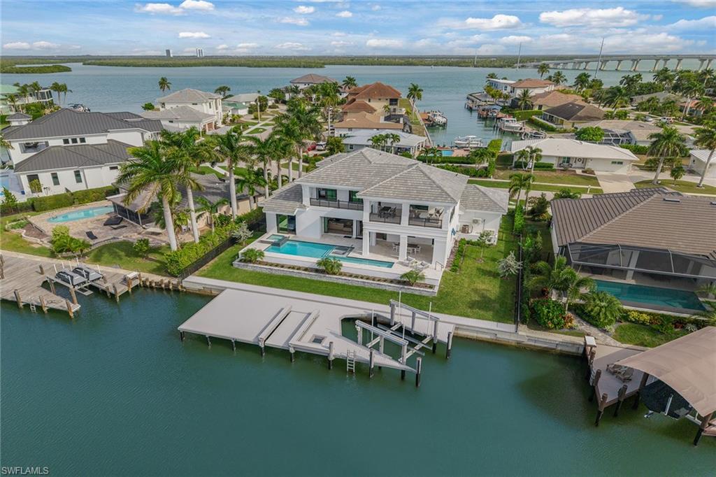 Newly built in 2025 and immaculate, this exceptional Marco Island waterfront residence delivers a better-than-new experience without the hassle or wait of building. Direct Gulf access, spectacular western sunsets and resort-style outdoor living complement its quality construction, exquisite designer furniture, decorator furnishings and statement lighting. Sure to impress even the most discriminate homeowner, carefully coordinated interiors pair elegant furniture and distinctive lighting with refined materials and architectural detail, creating spaces that feel luxurious and exceptionally inviting. Across two thoughtfully designed levels, impact glass, engineered wood flooring, crown molding, tray and coffered ceilings and built-in speakers create a sophisticated coastal setting. The dramatic entry leads to an open-concept living room featuring a shiplap accent wall and sleek electric fireplace and flows into the dining area and chef’s kitchen. Custom white cabinetry with LED accent lighting, quartz countertops and a herringbone tile backsplash showcase premium Thermador appliances, including a six-burner range, refrigerator, dishwasher and drawer microwave. A spacious island with hidden electrical outlets, walk-in pantry and pot filler blend style and functionality. The primary suite offers custom wall detailing, a tray ceiling and dual walk-in closets. Its spa-inspired bath features quartz vanities, dual porcelain undermount sinks, a white lacquer soaking tub and a walk-in shower with matte porcelain tile. Guest suites span both levels, each with an en-suite bath featuring quartz vanities, walk-in showers and curated designer tile. Upstairs, a spacious family room with a built-in bar and balcony access provides another inviting retreat. The waterfront lanai features porcelain tile flooring, tray ceilings, recessed LED lighting, ceiling fans, built-in speakers, electric screens and shutters. A lap pool with sun shelf and spa creates a private resort atmosphere, while the outdoor kitchen with Lynx grill, sink and beverage refrigerator makes sunset dining effortless. A 20,000-pound boat lift, kayak lift and direct access to the Gulf and island waterways offer exceptional boating convenience. Additional highlights include a pool bath, well-appointed laundry room and epoxy-finished three-car garage with LED lighting, mini-split system and flood vents. Marco Island, named No. 1 Island in the United States and No. 4 in the world in Tripadvisor’s Travelers’ Choice Island awards, offers beautiful beaches, waterfront and beachfront restaurants, boutiques, golf, tennis, pickleball and kayaking, plus a history museum, art center, theater, quality schools and nearby executive airport. Beautifully crafted and impeccably finished, this residence brings together designer elegance, waterfront recreation and unforgettable sunsets, ready to enjoy from the moment you arrive. Imagine living the ideal island lifestyle this coming winter!