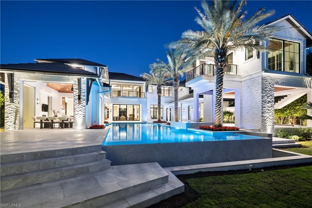 NOW COMPLETE! Commanding a rare western lakefront setting in the heart of Old Naples, this extraordinary new construction estate represents an exceptional achievement in architecture, craftsmanship and sophisticated resort-style living. Encompassing more than 9,400 square feet of interior living space, the residence was conceived as a private retreat where dramatic design and meticulous attention to detail come together effortlessly.

Twin infinity-edge reflecting pools create a striking arrival, leading into a soaring two-story great room defined by precision millwork, architectural symmetry and a sculptural floating staircase. The formal dining room is enhanced by a dramatic glass-enclosed wine wall incorporated into bespoke cabinetry, while the chef’s kitchen features Wolf and Sub-Zero appliances, dual Miele coffee stations and a concealed butler’s pantry designed for seamless entertaining.

The first-floor primary suite is a private sanctuary unto itself, complete with a dedicated study, two expansive dressing rooms, discreet laundry center and luxurious marble-clad bath with indoor and outdoor showers. Upstairs, five beautifully appointed bedroom suites are joined by a media lounge and concealed club room featuring a full bar and humidor.

Equally impressive outdoor spaces were designed to showcase the spectacular western lake views and Naples sunsets. A 60-foot negative-edge pool spans the rear of the residence, with dramatic stepping-stones crossing the water to a sunken firepit lounge. An elevated spa, expansive covered loggia and fully equipped summer kitchen create an extraordinary setting for outdoor living and entertaining. A detached fitness pavilion overlooking the lake provides another remarkable element to this private resort environment.

Additional features include an elevator, three laundry stations, commercial-grade sheet ironer, whole-home generator, comprehensive smart-home technology and a five-car split garage designed with the collector in mind.

Created by EMB Custom Homes in collaboration with MHK Architecture, Lotus Construction and Freestyle Interiors, and offered fully furnished, this newly completed lakefront estate presents a rare opportunity to experience exceptional scale, design and craftsmanship in one of Old Naples’ most coveted settings.