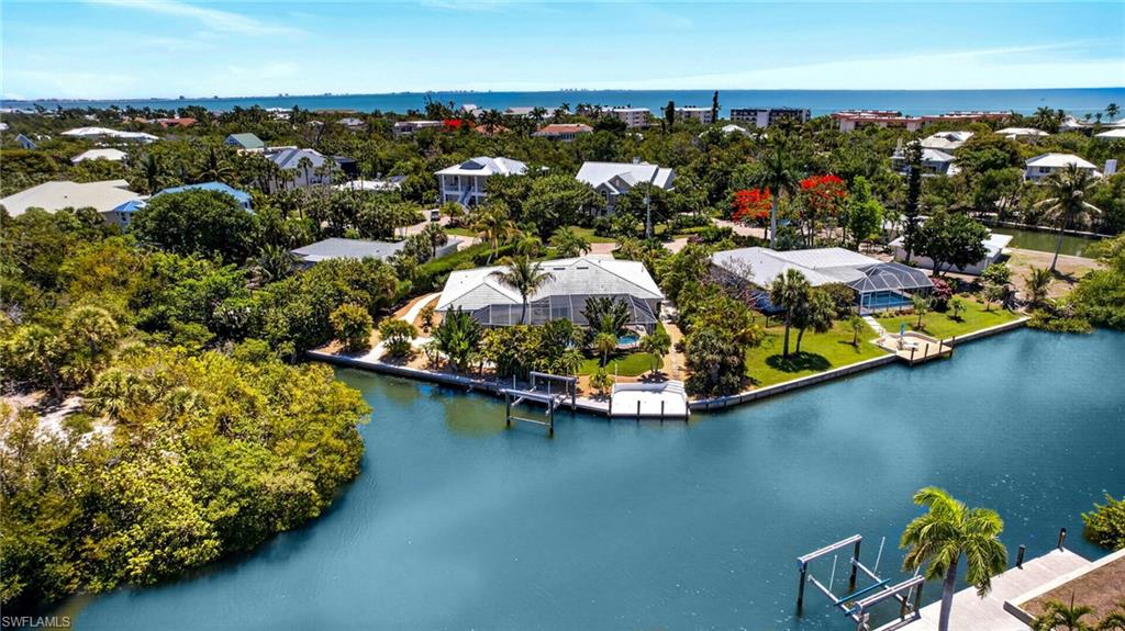 There are homes that impress, and there are homes that linger in memory long after the visit is over. The difference is often found in the details, the subtle nuances that quietly elevate a property from exceptional to irreplaceable. Along Sanibel Island’s desirable east end, this remarkable waterfront retreat is defined by those rare distinctions. Tucked away along the charming, tree-lined stretch of Anchor Drive, one of Sanibel’s sought-after streets, the setting alone is extraordinary. Unlike many island roads that simply end at the water, Anchor Drive transitions into a picturesque brick-paver lane leading to a private footbridge that gently crosses the canal and delivers residents directly to beach access beyond. It is a feature few properties on the island can claim, an effortless connection between boating and beach lifestyles, where morning bike rides to the Gulf and sunset visits along the sand become part of everyday life. Positioned at one of the desirable locations along the street, this exceptional residence commands a breathtaking setting where a serene mangrove-lined canal meets a wide sea walled canal, creating panoramic and breathtaking water vistas. With an impressive 180 feet of canal frontage, the property offers not only extraordinary privacy and scenery but also enhanced maneuverability, expanded dockage and direct boating advantages. The substantial private dock and lift can accommodate significantly larger vessels than most neighboring properties, delivering a yachter’s lifestyle with wonderful Gulf access. Surrounded by lush tropical landscaping and enveloped in complete privacy, the home itself has been beautifully reimagined through an extensive remodel that blends refined island elegance with relaxed coastal sophistication. Thoughtfully curated interiors are complemented by designer furnishings, inviting gathering spaces and richly appointed finishes throughout. Expanses of beautiful flooring guide you through multiple living and sitting areas designed equally for intimate relaxation and effortless entertaining. At the center of the home, a stunning chef’s kitchen with an expansive island serves as the natural focal point, seamlessly connecting the interiors to the spectacular outdoor setting beyond. Walls of impact glass draw the eye outward to the screened pool enclosure, tranquil waterways and swaying tropical landscape, creating a constant sense of connection to the island’s natural beauty. This is more than a waterfront home. It is a rare convergence of location, boating access, beach proximity, privacy and lifestyle, the kind of property whose value reveals itself not in a single feature but in the extraordinary way every element comes together.