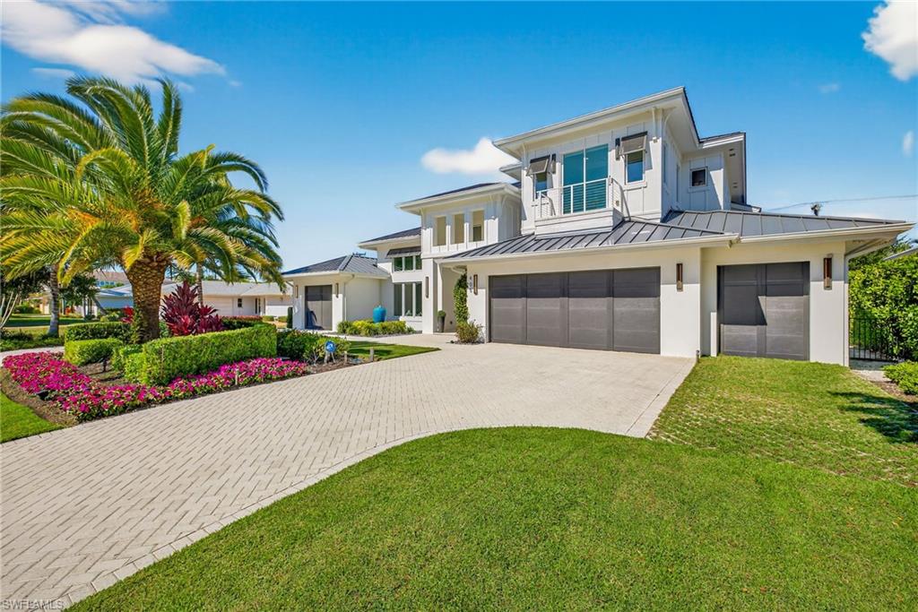 An extraordinary expression of modern coastal luxury, this architecturally striking residence enjoys an enviable location just two blocks from the pristine shores of the Gulf. Conceived through the creative collaboration of Integral Builders, Lotus Architecture, and L1 Design, this exceptional two-story home offers 4,100 square feet of beautifully curated interiors, where sophisticated design, dramatic architectural elements, and effortless indoor-outdoor living come together in perfect harmony. Originally created as a model residence, the home showcases an impressive collection of designer finishes and distinctive details throughout. A spectacular entry reveals soaring 22-foot ceilings, expansive walls of glass, and an abundance of natural light, establishing an immediate sense of grandeur. The dramatic great room, anchored by a statement fireplace and architectural feature wall, flows seamlessly into an elegant dining area and a stunning chef’s kitchen appointed with premium Wolf and Sub-Zero appliances, a magnificent waterfall-edge island, custom cabinetry, and a generous walk-in pantry. The thoughtfully designed main level includes a luxurious primary retreat featuring distinctive shiplap ceiling accents, dual closets, a spa-inspired bath, and private terrace access. An additional guest suite and a beautifully appointed study with sliding barn doors provide exceptional comfort and versatility. Upstairs, two spacious en-suite guest bedrooms are complemented by an inviting loft lounge and a private balcony overlooking the resort-style outdoor living area. Designed for year-round enjoyment and exceptional entertaining, the outdoor sanctuary features a covered lanai, inviting fireplace, fully equipped summer kitchen, and a spectacular pool and spa surrounded by lush tropical ambiance. A rare four-bay garage offers outstanding flexibility for automobile enthusiasts, recreational vehicles, or additional storage. Combining timeless architectural sophistication with the relaxed elegance of Naples coastal living, this remarkable residence presents an exceptional opportunity to enjoy refined luxury just moments from the beach, Four Seasons as well as 5th Avenue and 3rd Street renowned for its fine dining and shopping.