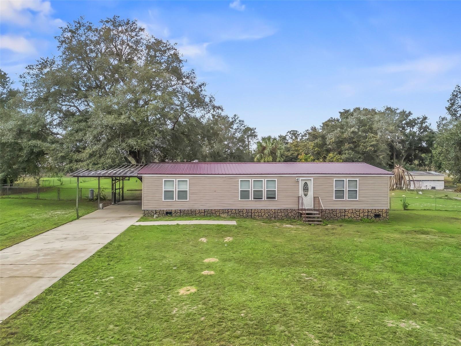 Spacious 1986 Doublewide Home on 1.06 Acres in Lovely Pines, Weirsdale! This well-maintained 2-bedroom, 2-bath home with a large den is situated on a beautiful 1.06-acre homesite in the Lovely Pines neighborhood. Conveniently located just off Highway 25, the property is within walking distance to Dollar General and only minutes from Lake Weir, Gator Joe’s, Eaton’s Beach, Circle K, the VA Hospital, The Villages, and other local amenities. Inside, the home features an open and spacious layout with drywall-finished interior walls, vaulted ceilings, ceiling fans, and vinyl flooring throughout. The kitchen offers a gas range, oak cabinetry, laminate countertops, and an adjoining dining area. A cozy fireplace enhances the living space, and the home includes an interior laundry room for added convenience. The primary bedroom is generously sized and includes a built-in media cabinet. A barn door leads to the primary en-suite bathroom, which features a shower and a vanity area. The guest bathroom offers a tub/shower combination, and the second bedroom includes a walk-in closet. Exterior features include a fenced backyard with chain-link fencing, a storage shed, an oversized Florida room, and a carport. The 1.06-acre lot provides ample outdoor space with mature oak trees offering shade and charm—ideal for pets, play, gardening, or relaxation. This property combines country living with close-to-town convenience. Schedule your showing today!