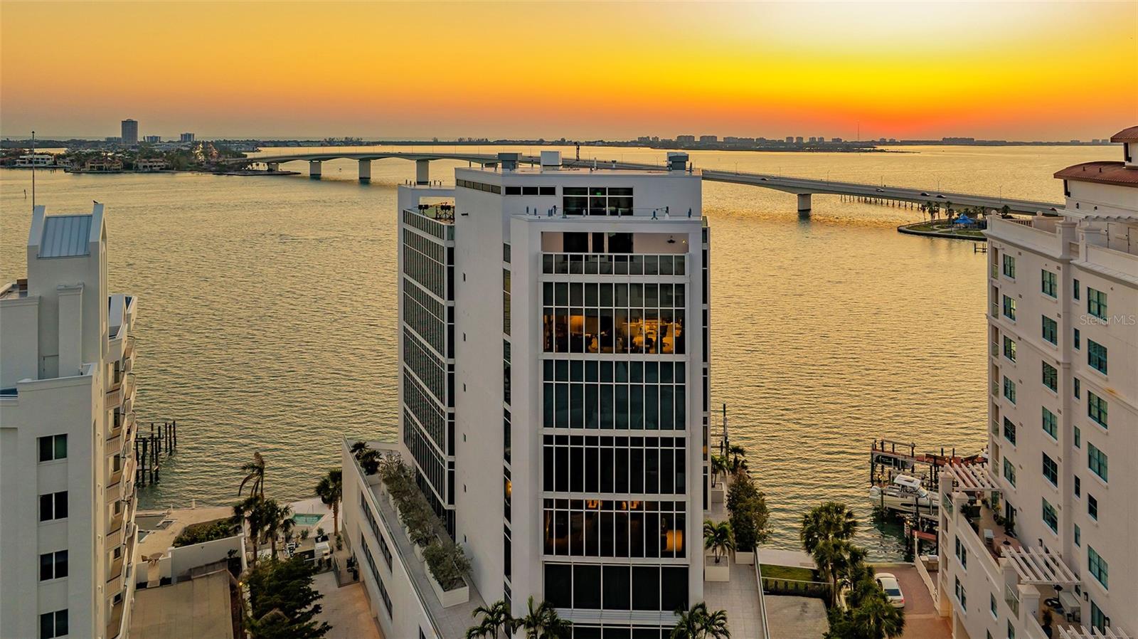 Architectural distinction meets breathtaking bayfront living at AQUA. Designed by renowned, award-winning Sarasota architect Guy Peterson, this exceptional full-floor residence is one of just eight residences in AQUA, an exclusive boutique tower on Golden Gate Point. Positioned on the sixth floor, this 4,100+ square-foot condominium captures sweeping 180-degree views of Sarasota Bay and the iconic Ringling Bridge through expansive floor-to-ceiling glass throughout, creating a seamless connection between the sophisticated interiors and the surrounding waterfront landscape.  A private elevator opens directly into a welcoming foyer, revealing clean architectural lines, dramatic natural light, and a refined contemporary aesthetic. With more than $500,000 in carefully curated owner upgrades and barely lived in, this extraordinary residence offers a level of customization and sophistication rarely found in Sarasota. The open-concept floor plan lives like a single-family home, with generous entertaining spaces, a waterfront dining area, and a beautifully appointed custom wet bar.  The chef’s kitchen blends exceptional design with luxury appliances, including a Wolf cooktop and ovens, two Miele dishwashers, and a Sub-Zero refrigerator. Custom Cuisines Laurier cabinetry and an expansive nine-foot island topped with striking Cielo quartzite complete this impressive culinary space.  The private primary suite serves as a peaceful retreat, with captivating bay views and custom walk-in closets featuring sleek Cuisimax poly-gloss doors, two separate wardrobe sections, and a dedicated packing station. The spa-inspired primary bath features dual vanities topped with stunning azure crystal marble, a soaking tub, and an oversized glass-enclosed shower. Two additional guest suites offer en-suite privacy, while a separate office provides flexibility as a potential fourth bedroom.  AQUA delivers an exceptional collection of boutique amenities, including discreet concierge services, an oversized enclosed private two-car garage with EV charging and a dehumidifier, a private boat dock accommodating a 36-foot vessel, a flat kayak lift, temperature-controlled wine storage and tasting room, fitness studio, heated pool and spa, and meeting room.  Ideally situated on Golden Gate Point, this remarkable residence offers the best of both worlds: a quiet, private waterfront setting just moments from the restaurants, galleries, and cultural attractions of downtown Sarasota.
