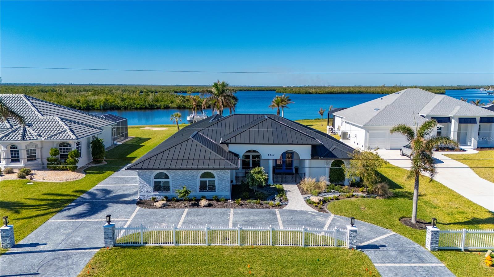 Craftsmanship, scale, and exceptional boating access come together in a Port Charlotte waterfront residence designed with remarkable attention to detail. Set on more than half an acre with 97 feet of waterfront, this 4 bedroom, 3.5 bath home with a 3 car garage captures serene lagoon and mangrove-lined views from the main living areas and lanai, while direct sailboat access with no bridges leads through Manchester Waterway to Charlotte Harbor and the Gulf. A circular driveway introduces an interior where custom design takes center stage. Rich woodwork, distinctive fixtures, custom barn doors, Chicago brick accent walls, and tile flooring throughout give the open-concept living spaces a sophisticated yet comfortable character. Every element feels purposeful, creating a home equally suited for refined entertaining and relaxed everyday living. The gourmet kitchen serves as a striking centerpiece with a seamless island and breakfast bar, dual ovens, pull-out microwave, wine refrigerator, custom coffee bar, and a walk-in pantry finished with a designer door. Nearby, the expansive dining area features a built-in dry bar, while a separate library or office provides an intimate space for work, reading, or quiet retreat.
The primary suite offers its own sense of understated luxury with exposed beams, private lanai access, and a spa-inspired bath featuring custom cabinetry, a spacious walk-in shower with dual showerheads, and beautifully selected finishes. Guest accommodations were designed with flexibility in mind. One bedroom includes a Murphy bed, while another area offers two rooms divided by a sliding barn door along with a bathroom, allowing the space to adapt for guests, multigenerational living, an additional bedroom arrangement, or a private sitting area. The outdoor living spaces continue the home’s polished design. Updated in 2022, the lanai features new pavers, a heated pool and spa, remote-controlled shades, and a convenient poolside half bath. Beyond the screened living area, the lagoon and mangrove-lined waterway create a peaceful, private backdrop for entertaining, fishing, or simply enjoying the setting. A newer composite dock with a 10,000-pound boat lift and seating area places the boating lifestyle directly at your back door. From here, enjoy no-bridge sailboat access through Manchester Waterway to Charlotte Harbor and beyond to the Gulf. Additional features include a 2022 metal roof, hurricane-impact windows throughout, and no past flooding. Set within a small, deed-restricted HOA community, this distinctive Port Charlotte waterfront home offers a rare combination of custom craftsmanship, more than half an acre of land, 97 feet of waterfront, and exceptional Gulf-access boating.