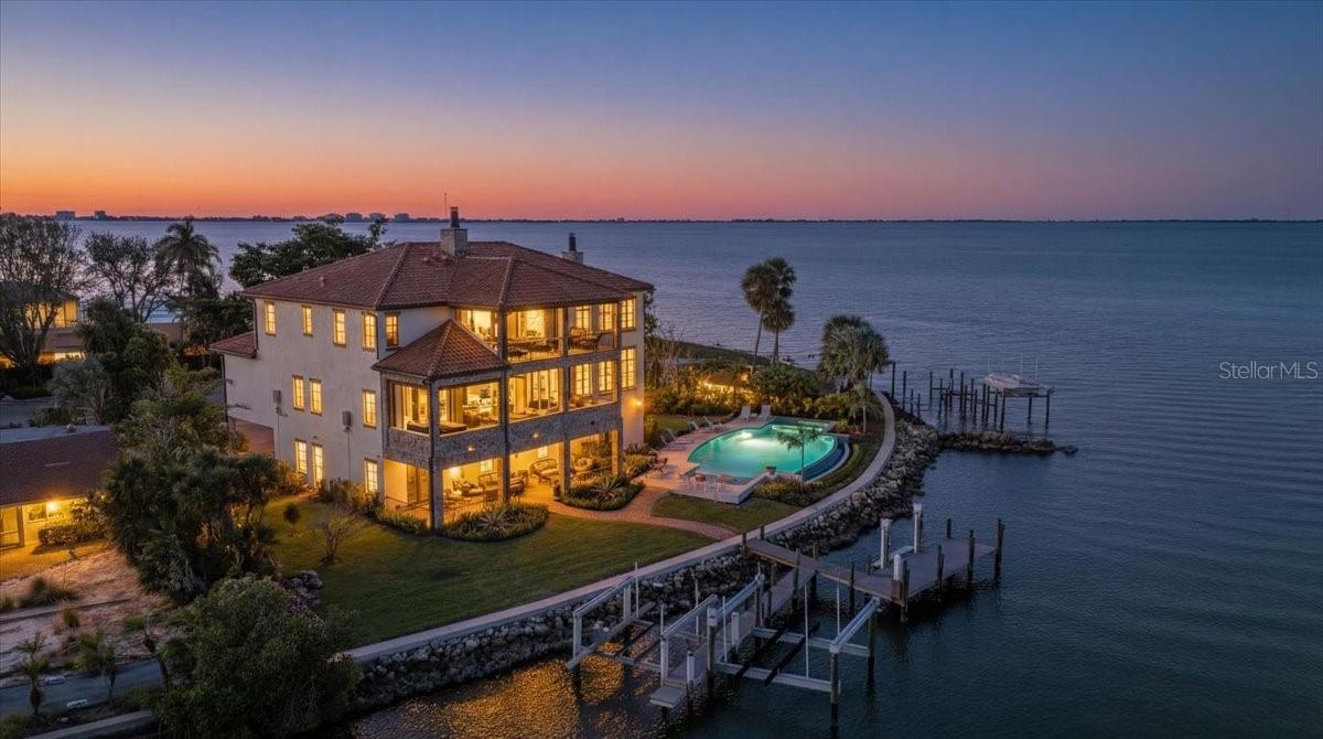 House never flooded, including during Hurricanes Milton and Helene, and protected by a generator! Built as a solid concrete structure on concrete pilings, this home was engineered for the Florida waterfront. Lavishly embellished with Old World authenticity, this exceptional waterfront estate evokes the grandeur of a 17th century Tuscan farmhouse. Custom built by John Cannon, the home is set on what was once Ringling’s personal yacht basin, offering protected sailboat water, 178 feet of seawall, a private dock, two boat lifts (24,000 lbs & 10,000 lbs), and a dedicated kayak lift platform, all framed by sweeping panoramic water views. From the moment of arrival, the level of craftsmanship is unmistakable. Walls are finished in aged plaster, hand made terra cotta floors have been acid washed and stained to reflect centuries of wear, and authentic frescoes and ceiling beams inspired by the Renaissance period add depth and character throughout. The great room provides a dramatic setting for entertaining with soaring 22 foot ceilings, a gas fireplace, and a wet bar accented by a hammered copper sink. The chef’s kitchen is equipped with an Italian eight burner gas range and Brazilian soapstone countertops, while the dining room features a rare brick vaulted ceiling that reinforces the home’s Mediterranean soul and creates a truly immersive dining experience. The primary suite is a romantic retreat with his and hers walk in closets and a spa like bath wrapped in rich wood and stone finishes. Additional spaces include two to three guest bedrooms, dual offices, a bonus room, and a wine room. A private elevator connects every level, offering effortless access from the garage to the living spaces above. A true 2,500 square foot ground level garage offers tandem parking for four plus vehicles, making it a dream for car collectors. Outdoor living is exceptional, with stone and wrought iron terraces, an outdoor kitchen and bar on the main level, all designed to capture natural breezes and expansive water views. The newly completed infinity edge pool and spa create a striking visual effect, with the water appearing to seamlessly spill into the bay. This storybook residence is ideally located near Sarasota’s beaches, dining, and cultural attractions, offering a rare blend of architectural artistry, privacy, and timeless elegance.