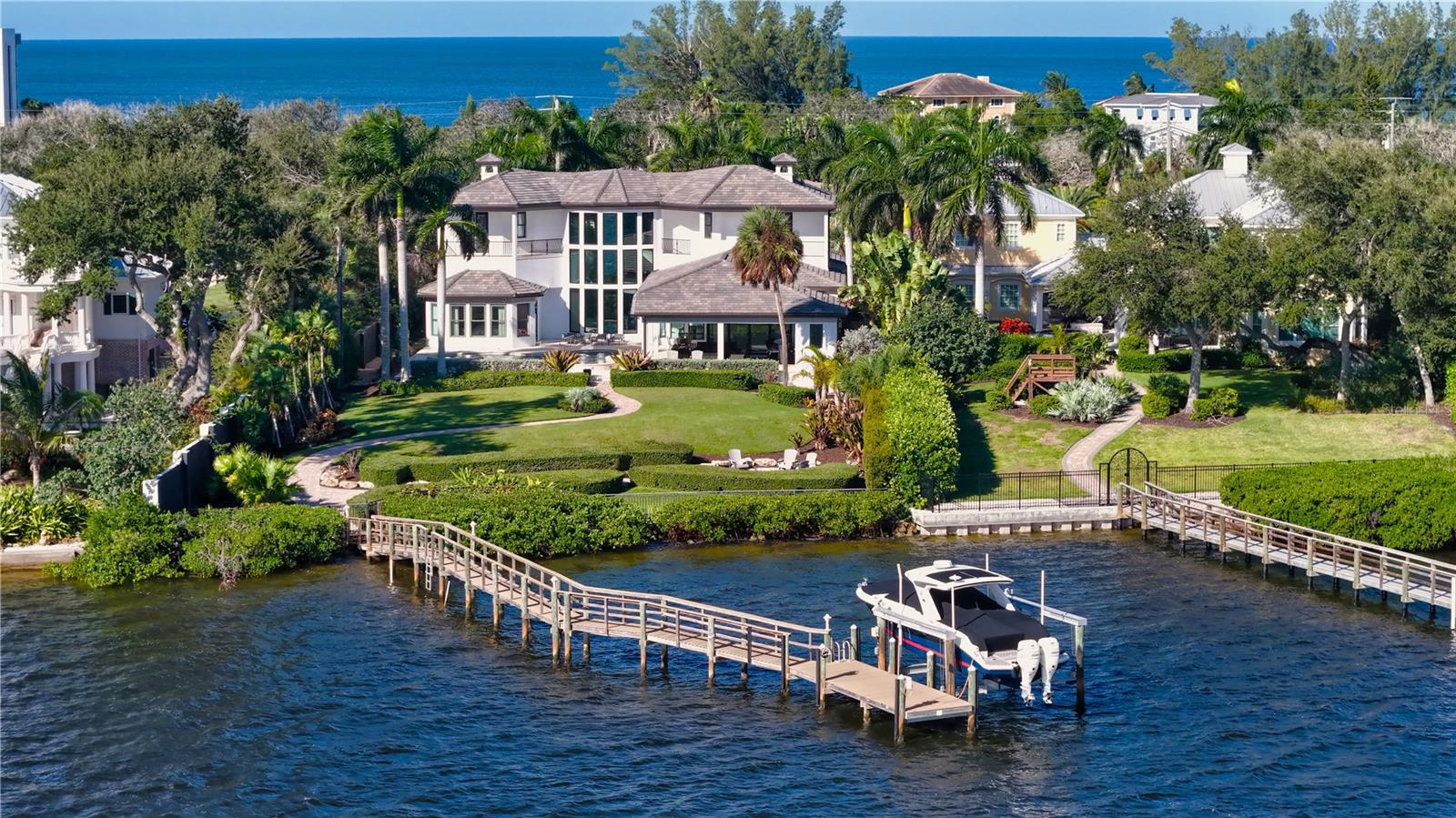 This private waterfront estate on Siesta Key combines modern Mediterranean architecture, beautifully updated interiors, and sweeping views of Little Sarasota Bay to create an exceptional coastal retreat. Set on over an acre of lush property behind a gated entrance and winding pavered driveway, this custom residence offers more than 100 feet of direct bay frontage, exceptional privacy, and unobstructed boating access to Sarasota Bay and the Intracoastal Waterway. Built in 2012 and extensively refreshed, the home encompasses more than 6,000 square feet of living space, four en-suite bedrooms, a four-car split garage, and an impressive collection of indoor and outdoor entertaining spaces. Offered fully furnished with contemporary pieces throughout, this remarkable home is ready for immediate enjoyment.
A dramatic entry introduces soaring cathedral ceilings, a neutral color palette, and walls of floor-to-ceiling glass framing the waterfront. The grand living room features a fireplace and spectacular two-story windows, while the adjoining formal dining room provides an elegant setting for entertaining. Tile flooring complements the main living level, with beautiful hardwood flooring upstairs.
The light-filled gourmet kitchen features quartz countertops, custom cabinetry, all-white appliances, gold fixtures, oversized center island, separate breakfast bar, dual built-in ovens, six-burner gas cooktop, and concealed 6-by-10-foot walk-in pantry. The adjoining informal dining area and spacious family room create an inviting gathering space overlooking the bay. Walls of pocketing glass sliders open completely to the covered outdoor cabana and fully equipped summer kitchen, seamlessly connecting indoor and outdoor living.
Privately positioned on the main level, the beautiful primary suite features peaceful water views, an oversized dual walk-in closet, and a luxurious marble-appointed bathroom. A nearby office/den offers a quiet retreat, while private access to the pool deck enhances the suite's connection to the outdoors. A secluded second en-suite bedroom with its own exterior entrance provides an ideal arrangement for guests or extended family. The first-floor laundry room offers generous built-in storage.
Upstairs, two spacious bedroom suites feature hardwood flooring, walk-in closets, updated en-suite bathrooms, and private balconies overlooking Little Sarasota Bay. An additional bonus room with dual closets and a wet bar overlooks the dramatic living room below and offers flexibility as a fifth bedroom, media room, or additional office.
Outside, lush tropical landscaping surrounds an expansive pavered pool deck with a heated swimming pool, raised spa, and covered outdoor living area. A waterfront firepit, private basketball court, and extended dock with a 20,000-lbs. lift complete this exceptional setting. Boaters will appreciate the property's 103 feet of shoreline and direct access to the open waters of Sarasota Bay. Recent improvements include a new roof in 2025, three updated bathrooms, and HVAC replacements in 2024 and 2022.
Ideally situated on Siesta Key, this private bayfront estate offers convenient access to Siesta Key Beach, Turtle Beach, Siesta Key Village, and the island's waterfront restaurants and recreational opportunities, just minutes away. Nearby mainland destinations include Downtown Sarasota, Marina Jack, Selby Botanical Gardens, renowned theaters, galleries, and cultural attractions.