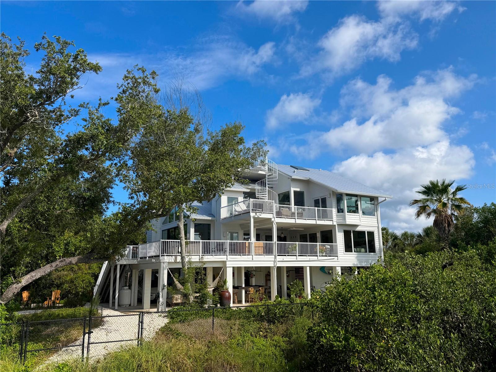Rare bayfront estate acreage on Manasota Key. This gated 6.39 acre property on Lemon Bay includes deeded Gulf beach access directly across the street, plus ownership of the natural shoreline and submerged lands extending into the bay, a private waterfront setting seldom available on the island.

The custom elevated residence offers 7,792 square feet under roof, with 3,806 square feet of conditioned living space and more than 2,000 square feet of decks and balconies. Finishes were selected at the highest level: Doca cabinetry, California Closets systems, Signature Kitchen Suite appliances, a Lutron lighting system, and new impact windows and doors by Jeld-Wen and Euro Wall.

The main living level opens to an expansive covered lanai finished in the same porcelain tile as the interior for seamless indoor-outdoor living. A main level suite with bay views, direct lanai access, custom closet systems, and a beautifully appointed bath offers flexibility for guests or multi-generational living. Upstairs, the primary suite opens to the upper deck and a rooftop observation deck with panoramic views of Lemon Bay, the Intracoastal Waterway, and the Gulf. A private elevator serves the home.

Outdoor living spans multiple levels: a ground level entertainment pavilion, outdoor kitchen and grill, fitness and recreation areas, a 10' x 8' spa, and a private boardwalk winding through the natural shoreline to a bayfront platform overlooking Lemon Bay.

Additional features include a metal roof, high efficiency mechanical systems, extensive insulation and air sealing, tankless propane water heating, and whole house water filtration, all beneath a canopy of live oaks and native palms preserved for privacy and beauty.

Sunrise over the bay and sunset over the Gulf, on a property of a scale and privacy that cannot be duplicated anywhere else.