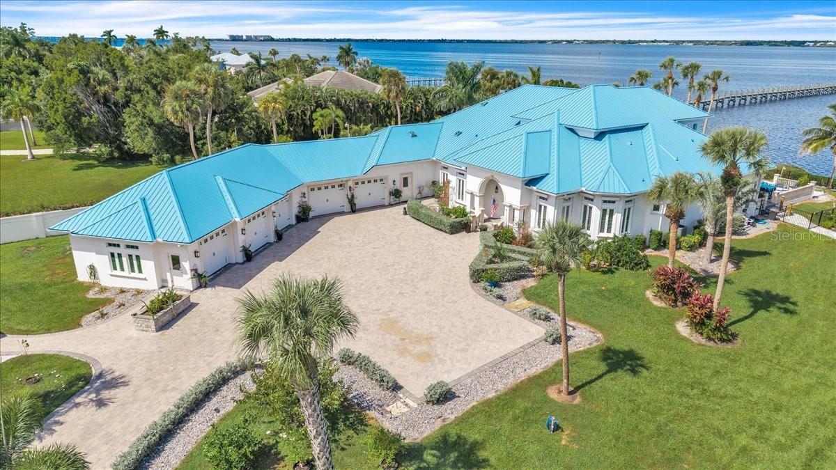 EXTRAORDINARY WATERFRONT ESTATE WITH PANORAMIC WATER VIEWS! Discover luxury, privacy, and coastal elegance in this magnificent 4-BEDROOM, 4-FULL-BATHROOM, 2-HALF-BATHROOM residence offering 5,061 SQUARE FEET OF LIVING SPACE, a 400-FOOT PRIVATE PIER WITH TWO BOAT LIFTS, and a 1,440-SQUARE-FOOT DETACHED SHOP/BARN WITH A/C UNITS! Surrounded by tropical landscaping and towering palms, this exceptional estate welcomes you through a private gated entrance and sweeping brick-paver driveway. A distinctive blue metal roof and elegant architecture create impressive curb appeal.

Step inside to a GRAND TWO-STORY LIVING ROOM featuring soaring ceilings, tile flooring, and a stunning curved staircase with wood handrails and decorative wrought-iron balusters. A second-floor overlook adds architectural elegance, while expansive windows fill the home with natural light.

The GOURMET KITCHEN features rich wood cabinetry, granite countertops and backsplash, stainless steel appliances, built-in double ovens, a center island, and glass-front display cabinets. AN OVERSIZED WALK-IN PANTRY provides extensive shelving and additional storage space. Enjoy casual meals in the separate dinette or entertain guests in the formal dining room.

The EXPANSIVE GREAT ROOM showcases tray ceilings, crown molding, recessed lighting, a fireplace with stone-look surround, and plantation shutters. Sliding glass doors open to the covered lanai for seamless indoor-outdoor living. A SEPARATE CUSTOM BAR AREA just off the kitchen features granite countertops, seating, wood cabinetry, a prep sink, and pendant lighting.

The thoughtfully designed floor plan includes TWO PRIMARY SUITES. The first-floor primary suite offers convenient main-level living and features an ADJOINING FLEX ROOM, perfect for a private home gym, home office, nursery, or additional sitting area. The second-floor primary suite, accessed by the curved staircase, features an ensuite bathroom, walk-in closet, and PRIVATE COVERED BALCONY WITH WATER VIEWS. Two additional first-floor guest bedrooms each have private ensuite bathrooms. A spacious laundry room with cabinetry, counter space, and a utility sink adds everyday convenience.

Step outside to a SPECTACULAR WATERFRONT OASIS designed for entertaining! The expansive covered lanai features multiple seating areas, ceiling fans, and a fire pit table, while an impressive OUTDOOR KITCHEN AND CUSTOM COVERED BAR boasts stainless steel cooking equipment, generous counter space, a sink, and bar seating overlooking the water. Enjoy the INFINITY-EDGE POOL AND RAISED SPA WITH CASCADING WATER FEATURES, surrounded by spacious paver decking and tropical landscaping. A private sandy beach area with Adirondack seating adds to the resort-style atmosphere, while the 400-FOOT PRIVATE PIER WITH TWO BOAT LIFTS completes this exceptional waterfront retreat.

Adding exceptional versatility is the 40kw generator and 1,440-SQUARE-FOOT DETACHED SHOP/BARN WITH A/C UNITS, featuring high ceilings, oversized garage doors, concrete flooring, overhead lighting, and generous workspace. Ideal for automotive enthusiasts, hobbies, boat storage, recreational equipment, or workshop projects.

A RARE OPPORTUNITY TO ENJOY LUXURY WATERFRONT LIVING WITH EXCEPTIONAL ENTERTAINING SPACES, PRIVATE BOATING AMENITIES, AND ROOM FOR ALL YOUR TOYS! For a complete list of this exceptional property's additional features and amenities, please see the FEATURE SHEET ATTACHED TO THIS LISTING.